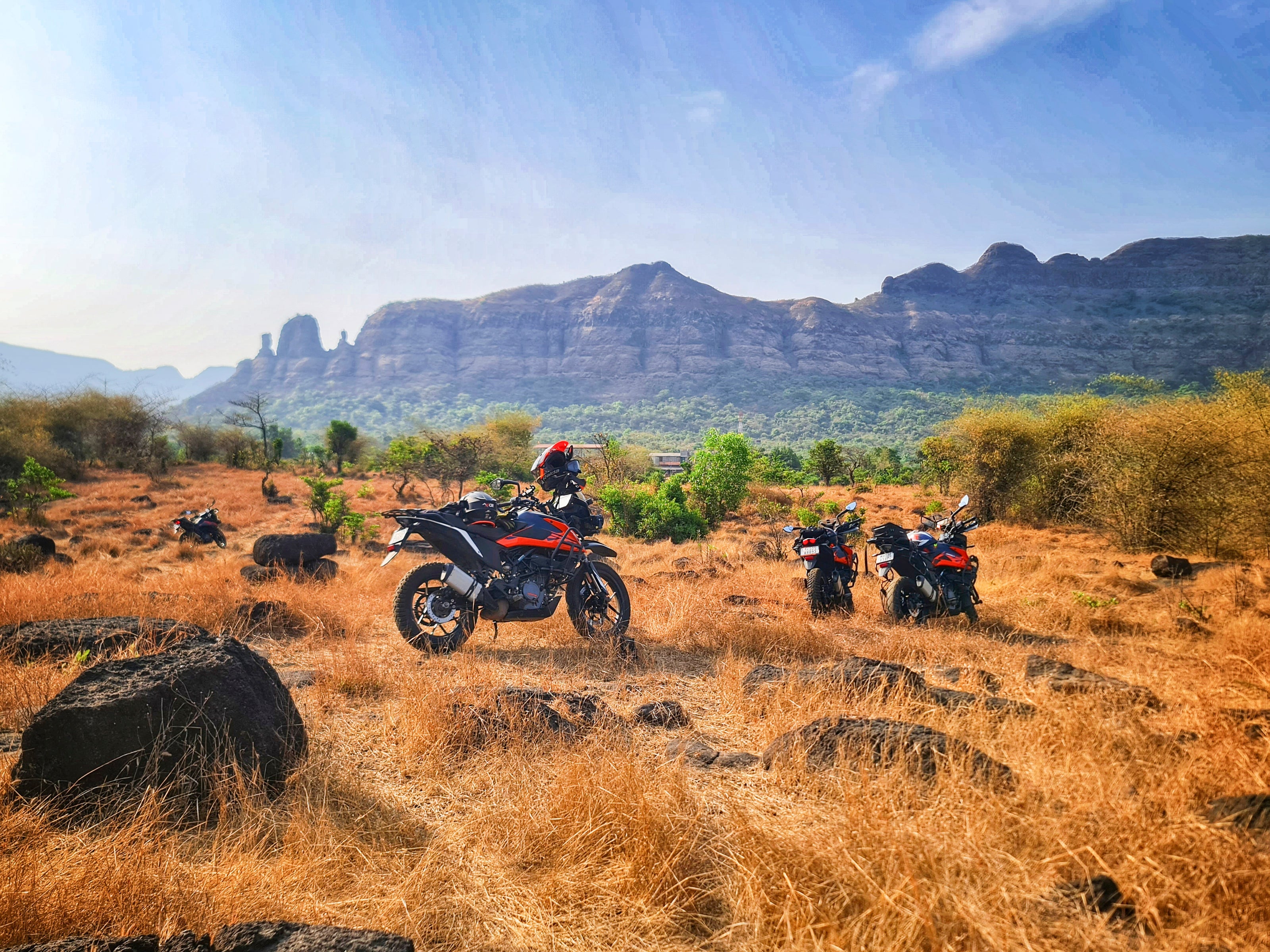 Adventure bike rider in full protective gear resting by a KTM motorcycle near a rocky lake with mountain views. Perfect shot of off-road touring, motorcycle travel, and outdoor adventure.
