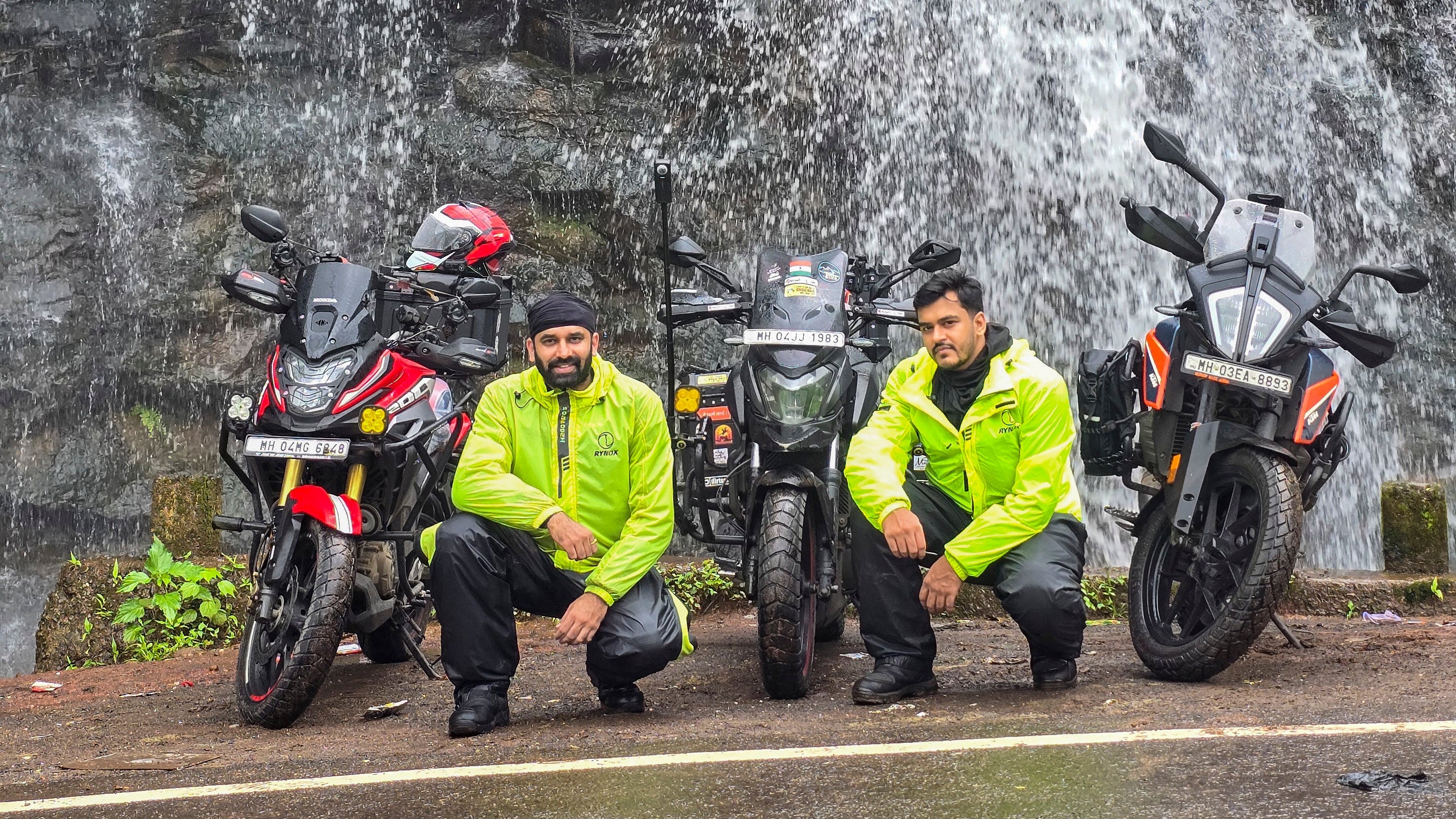 Two individuals in bright green jackets with motorcycles in front of a waterfall.